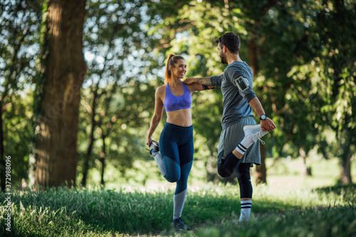 Side image of a young couple doing warming exercise in nature, they smiles and stick each other to maintain balance