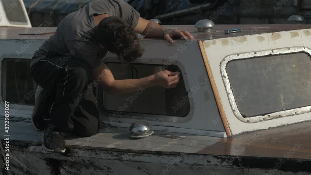 Young man removing sikaflex sealant flashing from aluminium windows Wooden boat Young man removing sikaflex sealant flashing from aluminium windows Wooden boat