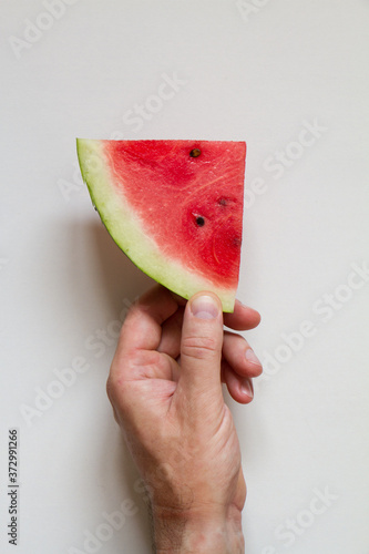 Male hahd holding slice of ripe watermelon on white background, top view photo