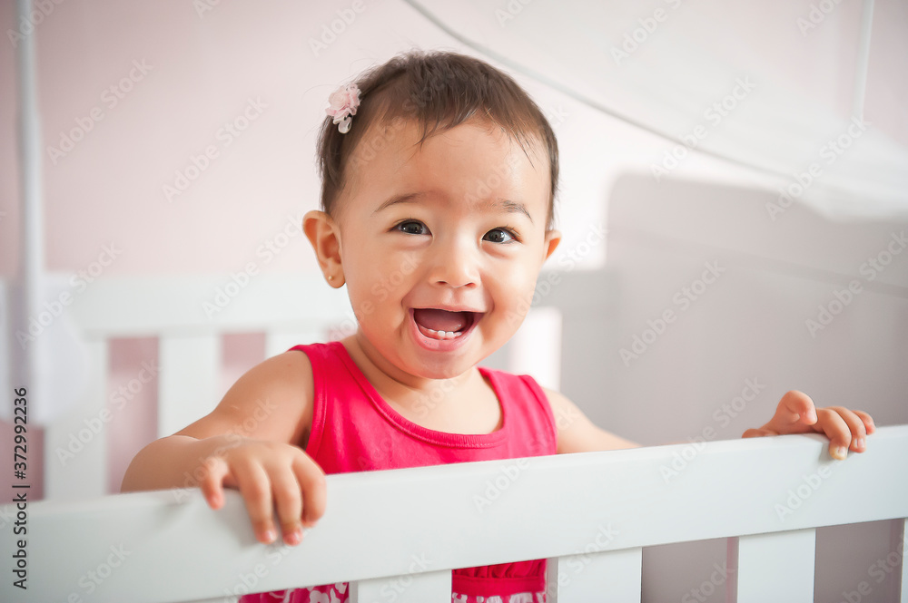 Beautiful child standing in crib smiling at camera. Seems to be screaming Beautiful child standing in crib smiling at camera. Seems to be screaming