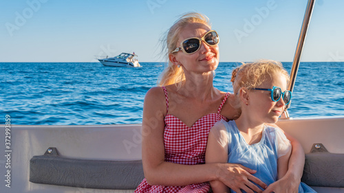 Smiling sits on a yacht, young with a kind look on the horizon of the sea, monochrome glasses, in the summer. Two Girls, Maam and Daughter photo