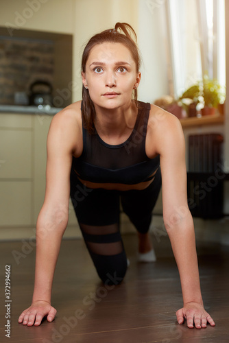 A sporty girl in a black workout tight pants and top is relaxing after doing push-ups at home. A woman is practicing exercises for the chest at her apartment.