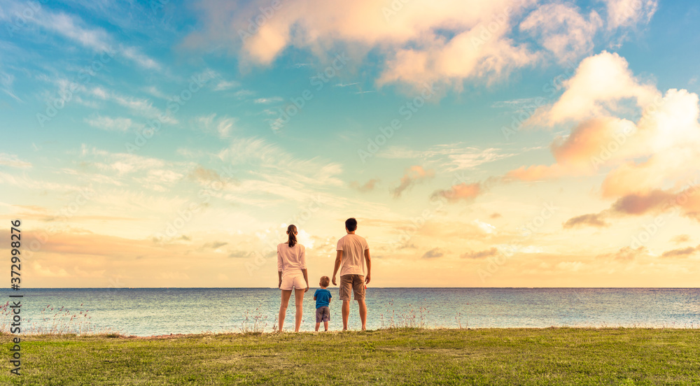 Fototapeta premium Family of three watching the sunset together holding hands. 