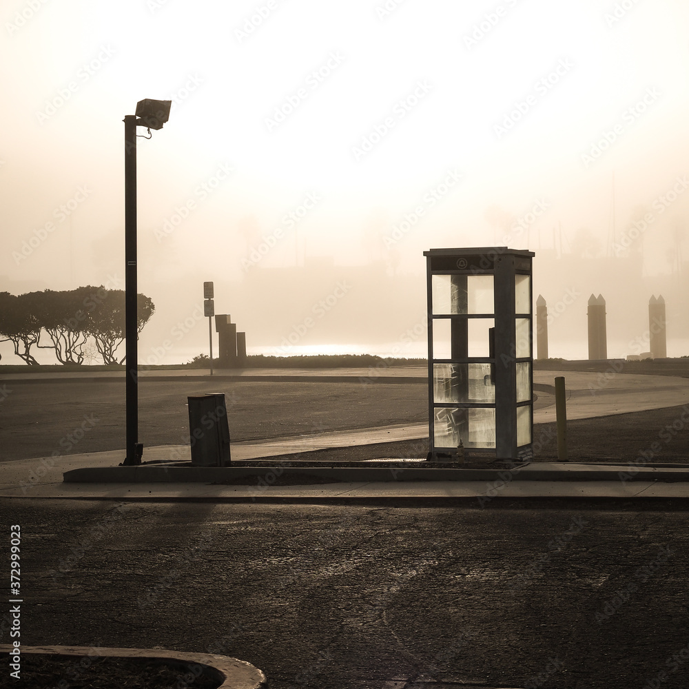 Abandoned phone booth in an empty parking lot on a foggy morning. Abandoned phone booth in an empty parking lot on a foggy morning.