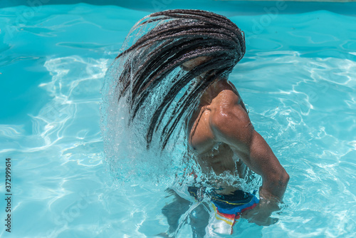 Young black man with dreadlocks inside a pool moving his wet hair in a trail of water photo