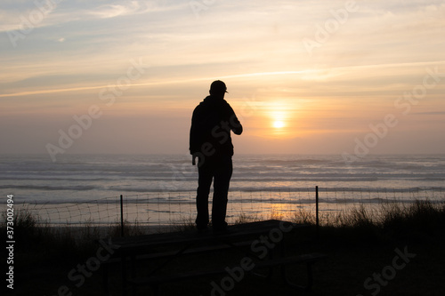 Man standing on a picnic table watching the sunset on an Oregon beach.