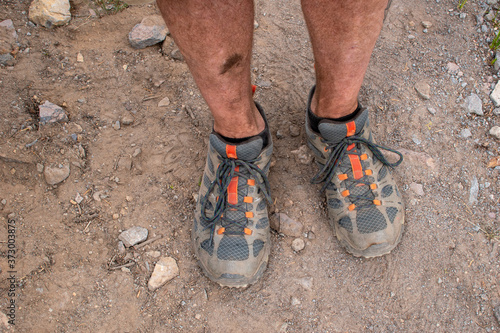 Dirty legs and hiking shoes on a hiker on a mountain trail, standing with feet slightly apart.