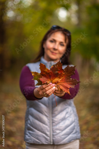 Portrait of woman holding a colorful maple leaf on natural background
