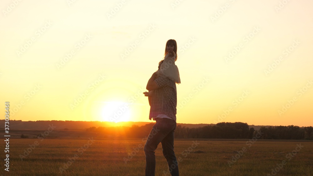daddy carries on the shoulders of his beloved healthy child in the sun. Father walks with his daughter on his shoulders in park. child with parents walks at sunset. happy free family concept