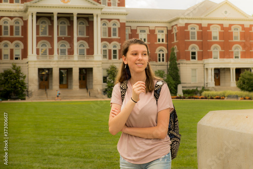 Environmental portrait of female student with backpack in late afternoon; Midwestern university building in the background