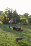 Tired woman making a short break while cutting grass with a lawn mower. Outdoor household chores concept.