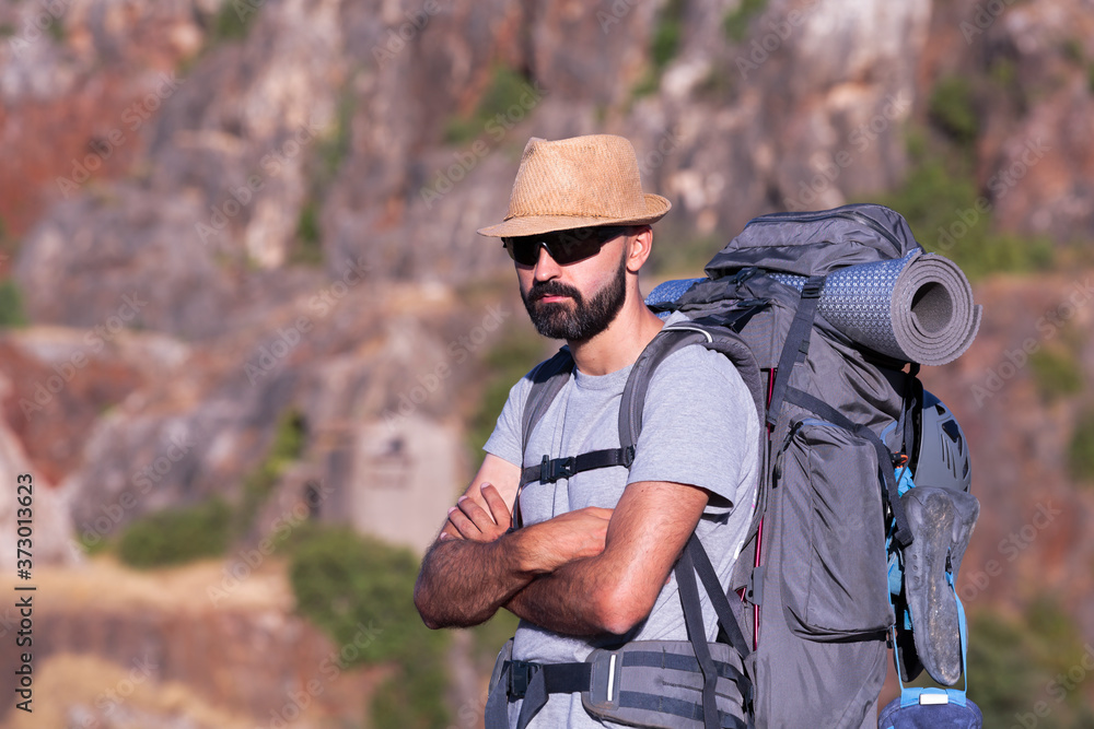 Horizontal view of a hispanic male trekker with sunglasses and a full backpack