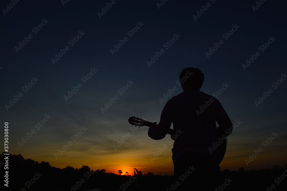 A man with a guitar strumming and looking at the sunset in the evening