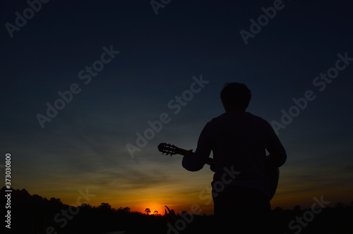 A man with a guitar strumming and looking at the sunset in the evening