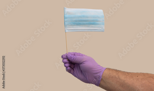 hand in a medical glove holds a flag. the flag is made from a surgical mask. photo