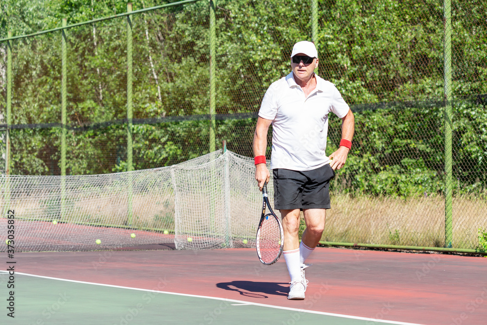 An elderly man plays tennis on an outdoor court
