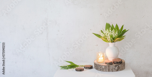 lily of the valley in vase with candles on background old white wall