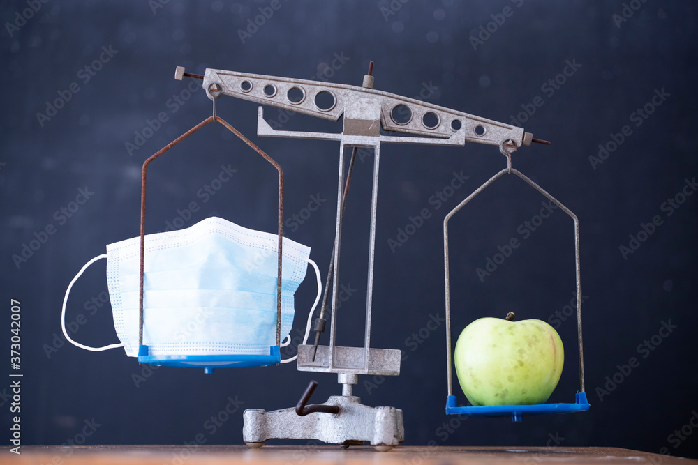 Balance with apple and medical mask, choosing between starting the school or stay at home.