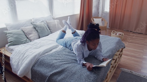 Attractive Young African American Woman lays in bed and reads the book