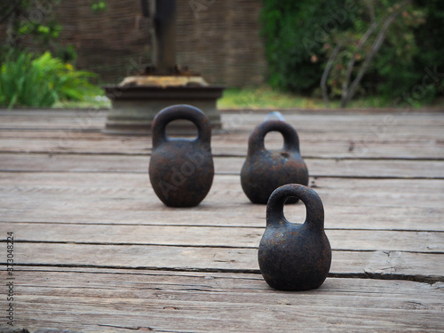 Fototapeta Naklejka Na Ścianę i Meble -  Outside, on a wooden platform, there are three round black dumbbells with a large, rust-stained handle. For sports - who is stronger.