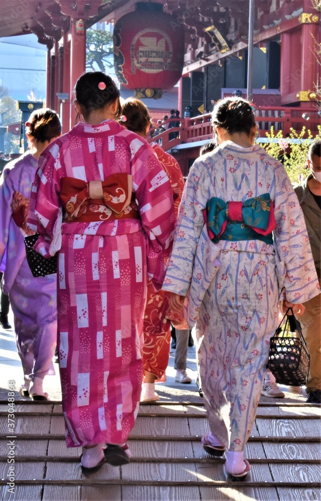 Young Asian women wearing traditional kimonos walk towards a temple