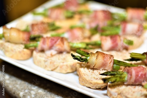 A plate of appetizers made of grilled asparagus spears wrapped in bacon and placed on top of small pieces of bread