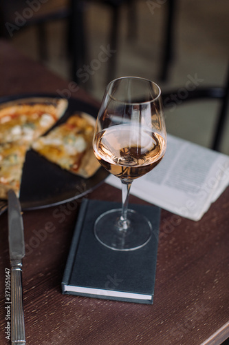 Close up of glass of rose wine with 4 cheese pizza and fresh newspaper on background at the cafe. Meal outside home. Leisure concept.