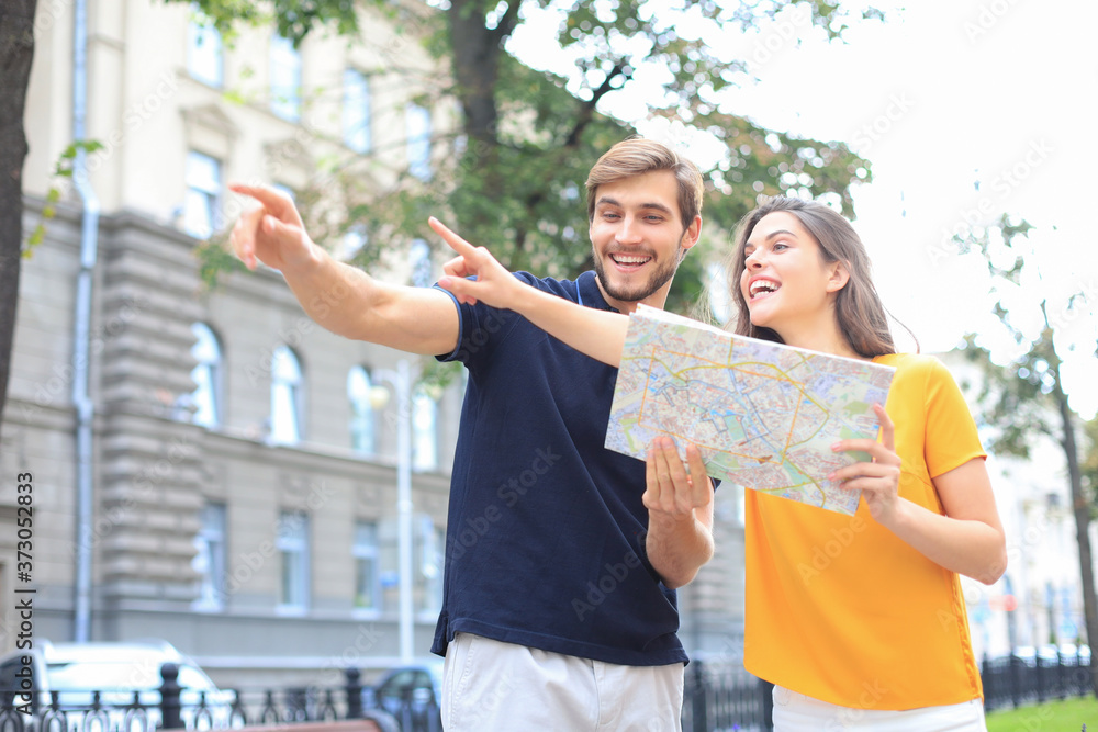 Naklejka premium Beautiful young couple holding a map and smiling while standing outdoors.