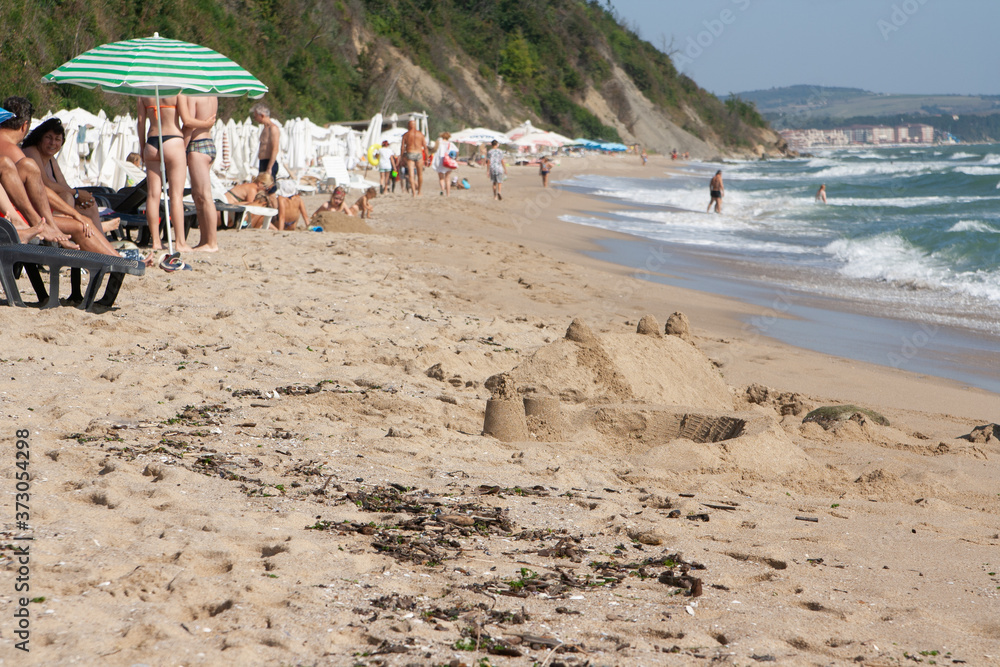 A beach with holidaymakers on the black sea and a sand castle in the foreground.
