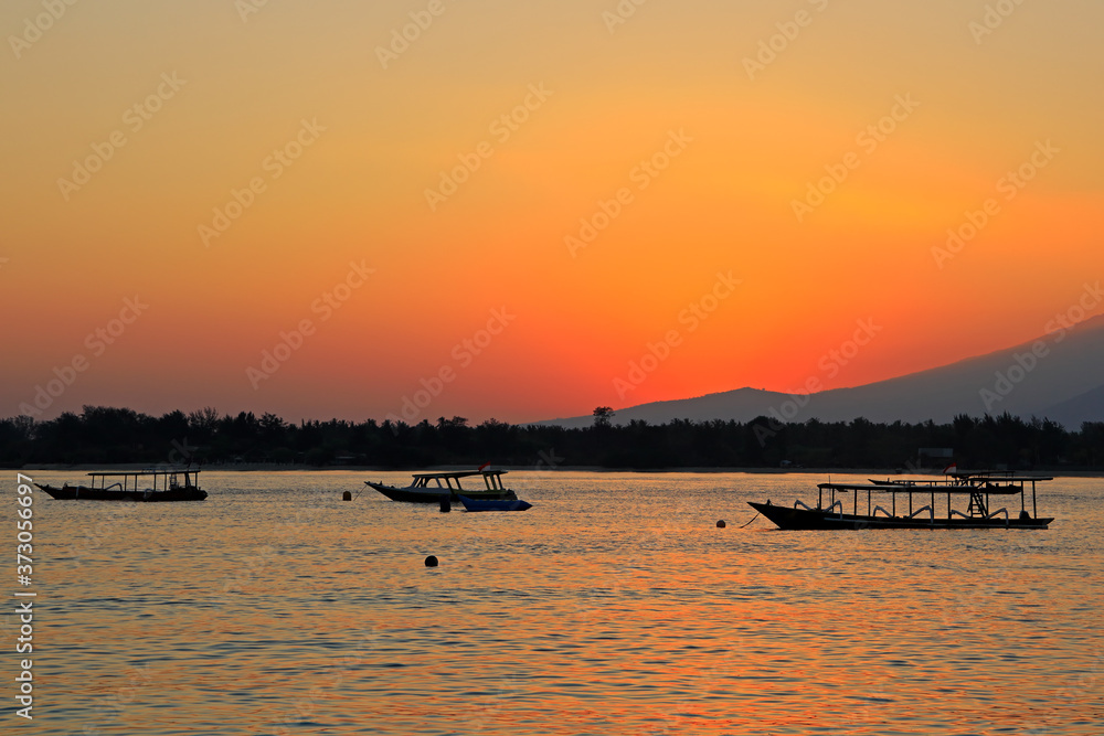 Scenic beach with boats silhouetted at sunset on a tropical island of Indonesia.