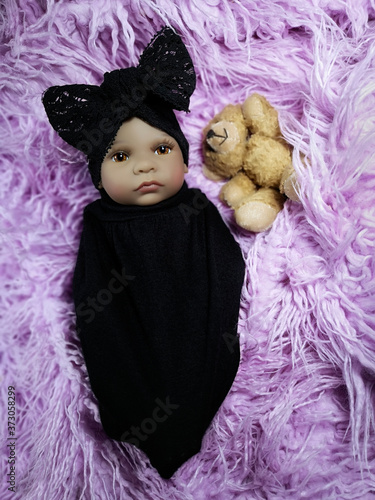фотографія Ethnic reborn baby doll in a  black set with teddy bear