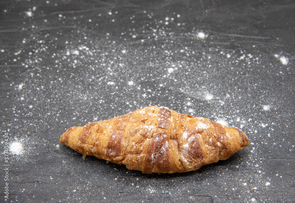 One croissant lies on a black slate background. One croissant lies on a black slate background.