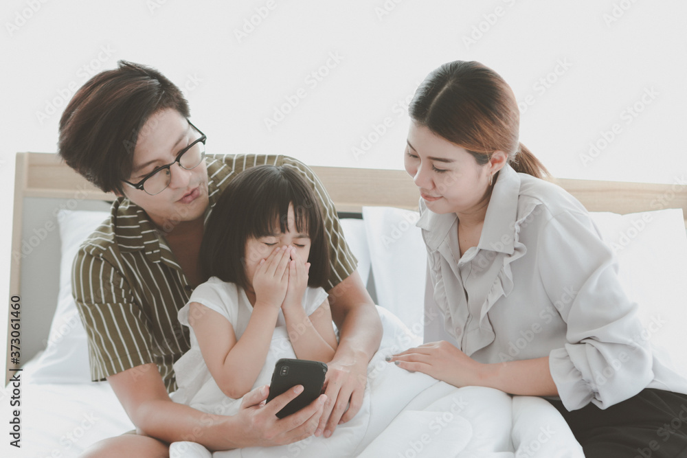 Happy family having fun in bedroom. Father, mother daughter spending time together, parents and kid having good memory together at home, girl sneezing while using mobile phone, allergy from dust Happy family having fun in bedroom. Father, mother daughter spending time together, parents and kid having good memory together at home, girl sneezing while using mobile phone, allergy from dust