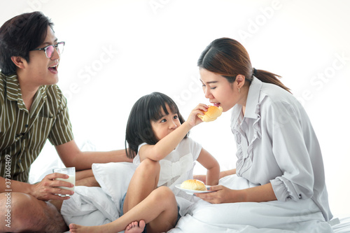 Happy family having fun in the bedroom. Father, mother, and daughter spending time together, girl giving bread to her mom for eating , parents and kid having good memory together at home