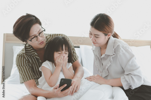 Happy family having fun in bedroom. Father, mother daughter spending time together, parents and kid having good memory together at home, girl sneezing while using mobile phone, allergy from dust
