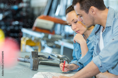 man and woman leaning on workbench conferring over designs