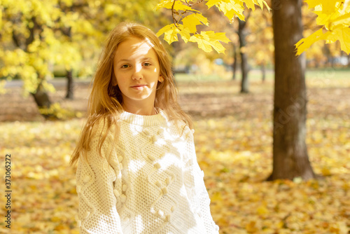 beautiful blonde teen girl walking in an autumn Park with maple trees