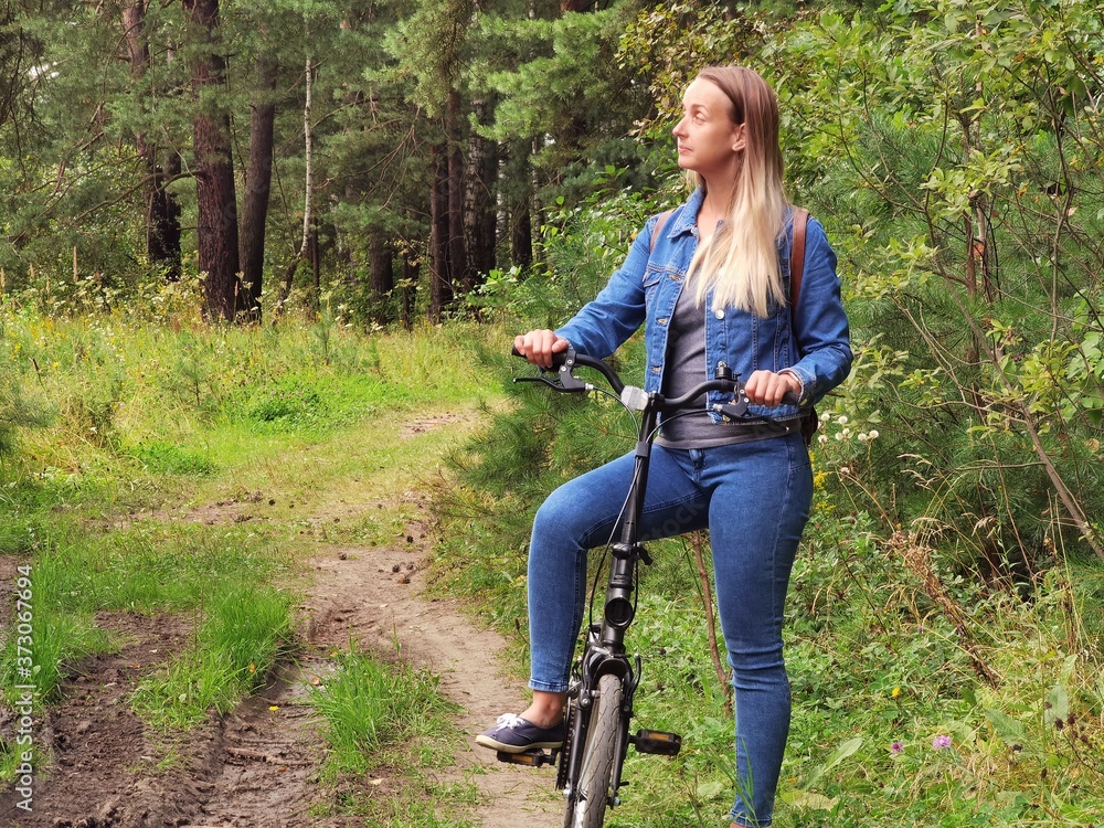 Woman in jeans riding on a bicycle at rural road Woman in jeans riding on a bicycle at rural road