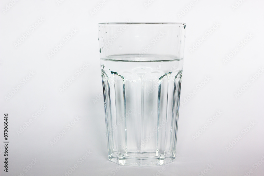 Pure drinking water in a glass cup. A stream of water and transparent droplets on the wall of the glass. Pour water on a white background. Pure drinking water in a glass cup. A stream of water and transparent droplets on the wall of the glass. Pour water on a white background.
