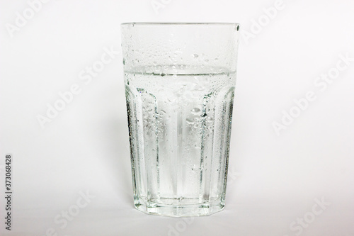 Pure drinking water in a glass cup. A stream of water and transparent droplets on the wall of the glass. Pour water on a white background.