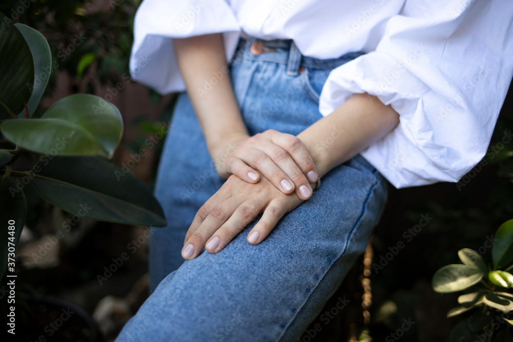 Young well-groomed hands with natural manicure of a girl in a white blouse and blue jeans. 
Beautiful female hands.