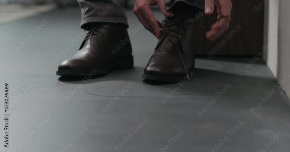 Slow motion dolly shot of young man unlace his brown leather chukka boots indoor Slow motion dolly shot of young man unlace his brown leather chukka boots indoor