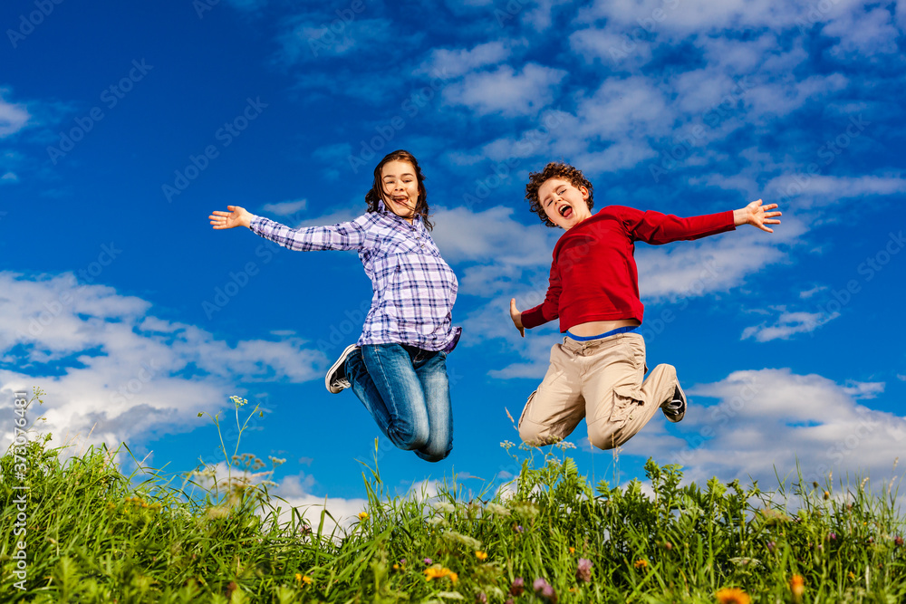 Girl and boy running, jumping against blue sky
Girl and boy running, jumping against blue sky