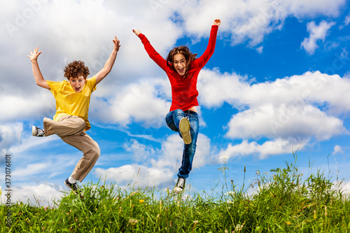Girl and boy running, jumping against blue sky 