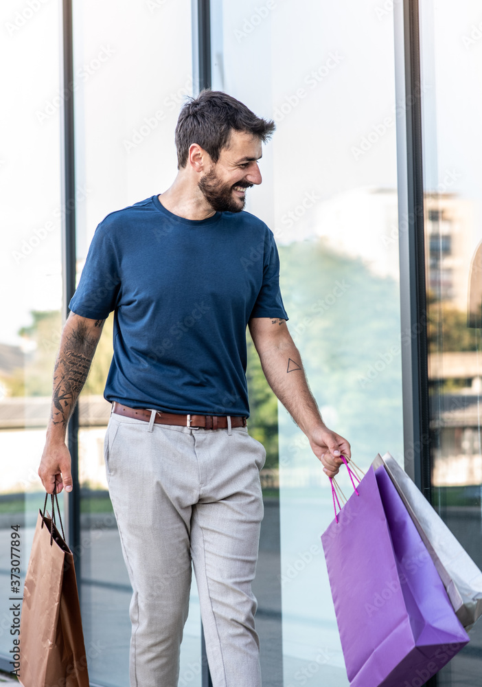 A young man walks next to shops and carries shopping bags with him, he saw something interesting in the shop window A young man walks next to shops and carries shopping bags with him, he saw something interesting in the shop window