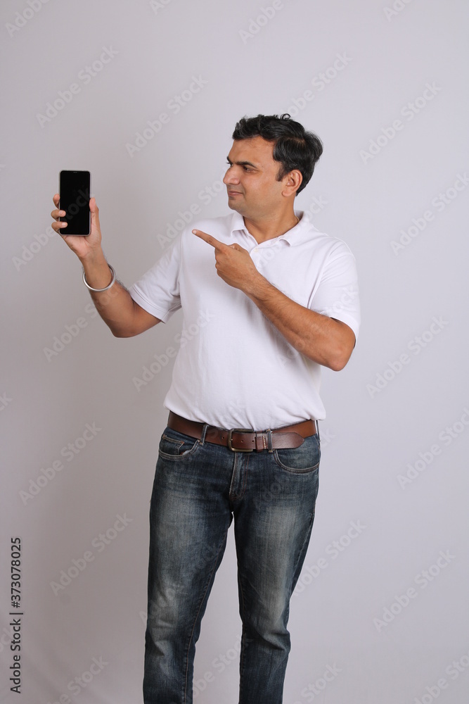 Young confidant Indian man pointing towards cell phone. isolated on white background. Young confidant Indian man pointing towards cell phone. isolated on white background.