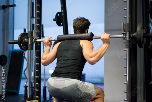 Man doing squats using a squat cage in a gym to train his legs