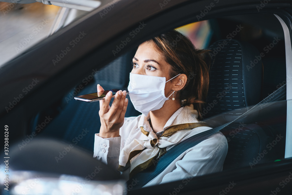 A young woman drives a car with a mask on her face and talks on a mobile phone, life during pandemic
