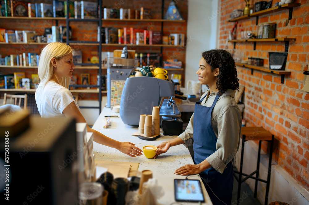 Female barista gives coffee to woman in cafe Female barista gives coffee to woman in cafe