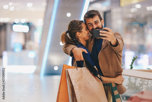 A couple satisfied with shopping is standing in the shopping mall and taking photos of them, they smiling